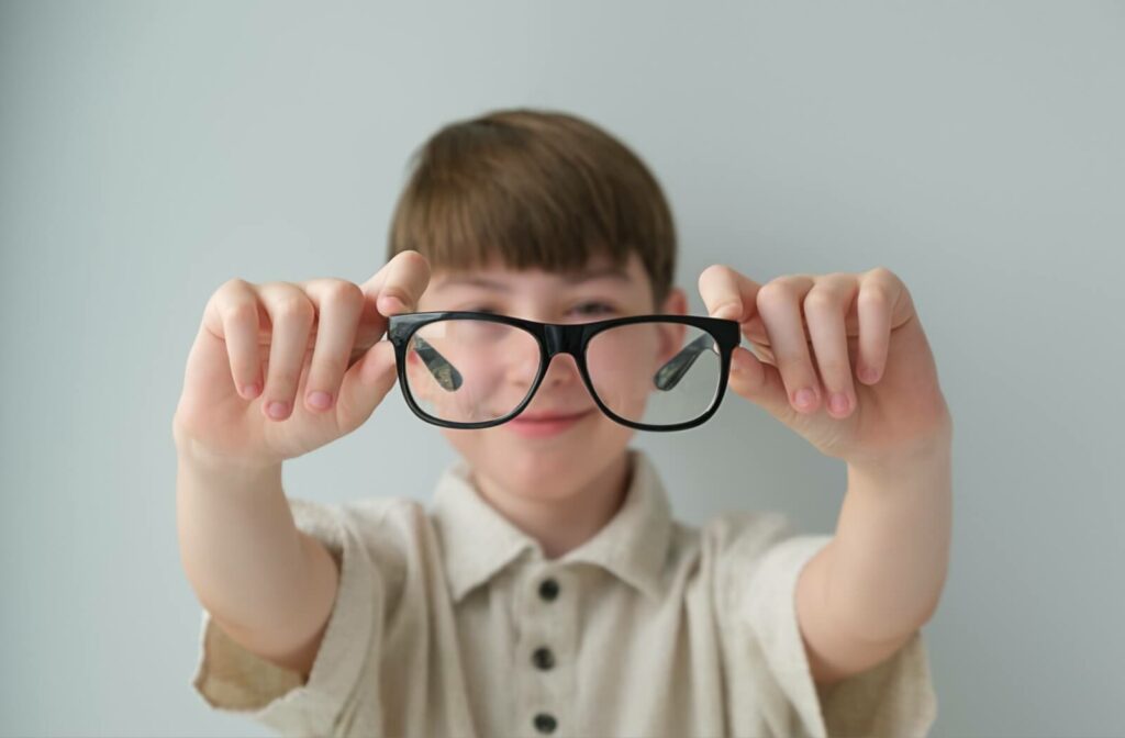 A child proudly holds up their myopia control eyeglasses with specially-designed lenses.