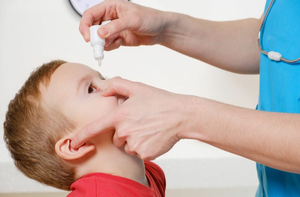 An optometrist places low-dose atropine eye drops into their young patient's eye for myopia control.